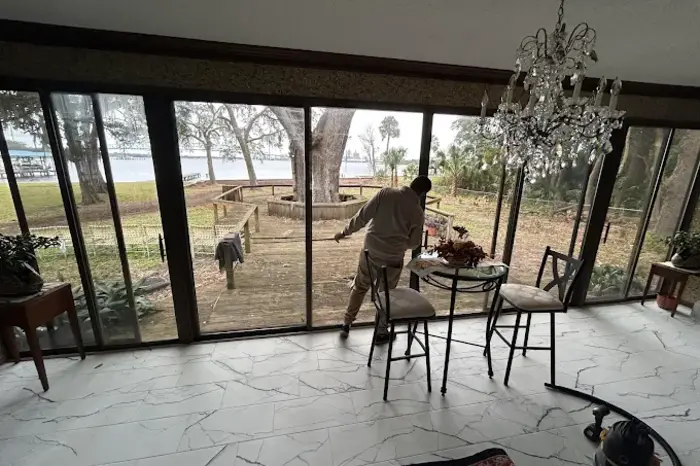 Technician servicing a wall of sliding glass panels in a lakefront Florida sunroom