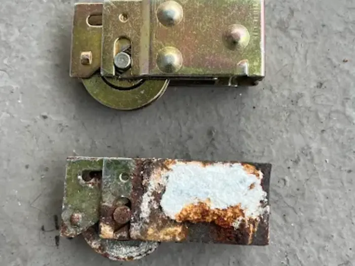 A shiny new sliding door roller next to a rusted, seized original roller